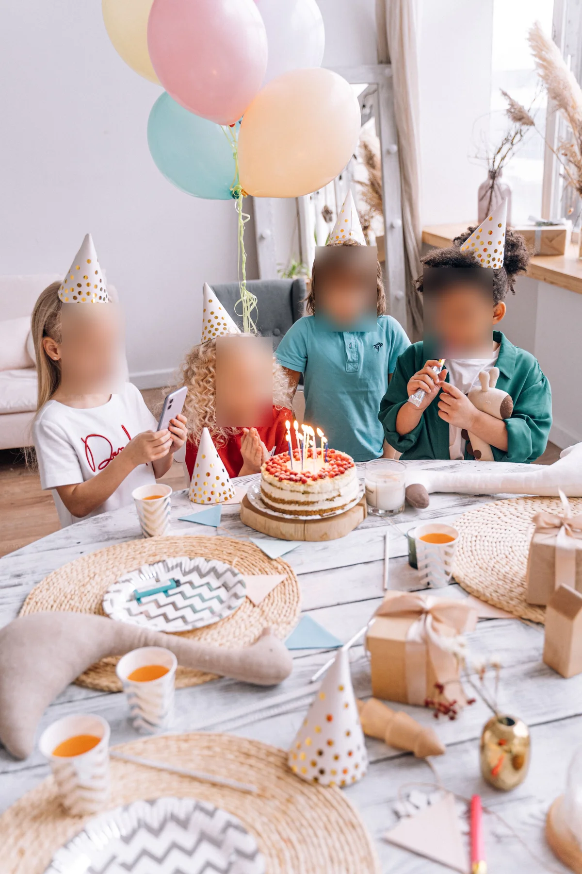 Four children at a birthday party with balloons and a cake, all four faces blurred while the cake, balloons and table stay untouched